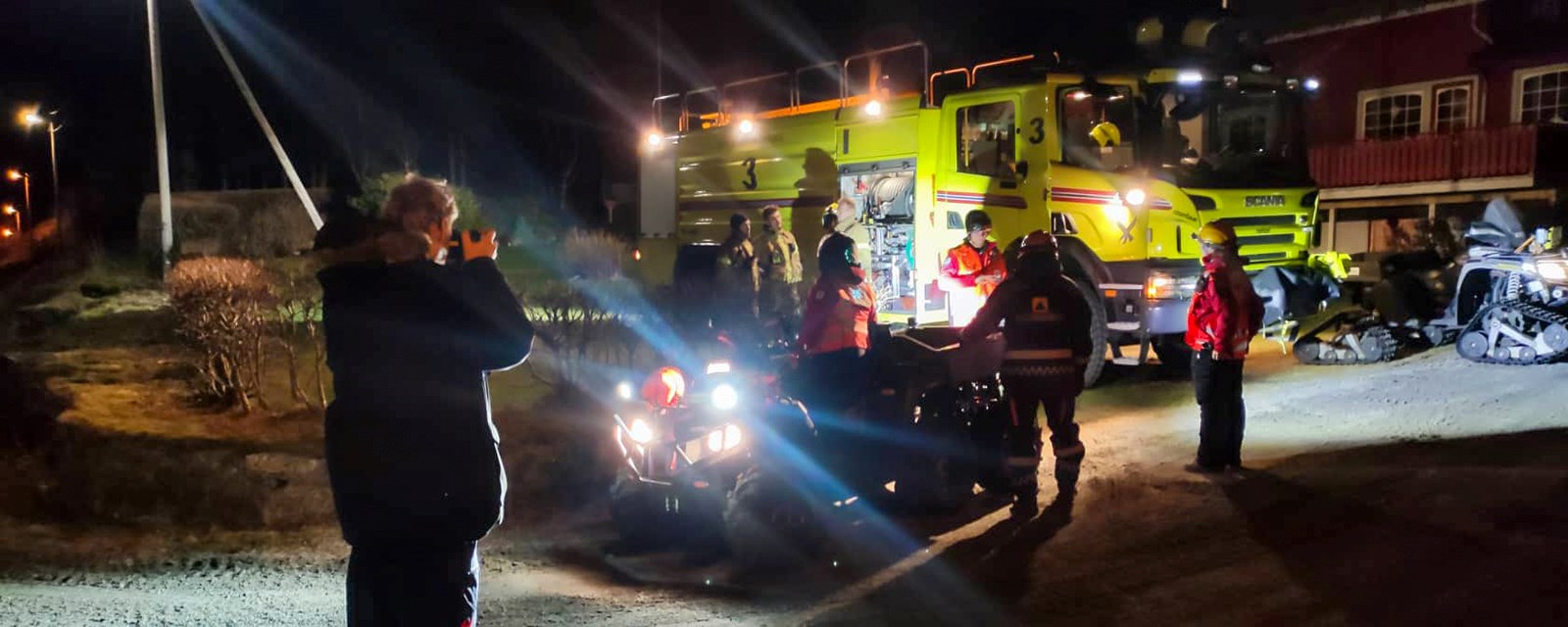 Mannskaper fra brannvesen og Røde Kors står rundt ATV og brannbil i mørket.