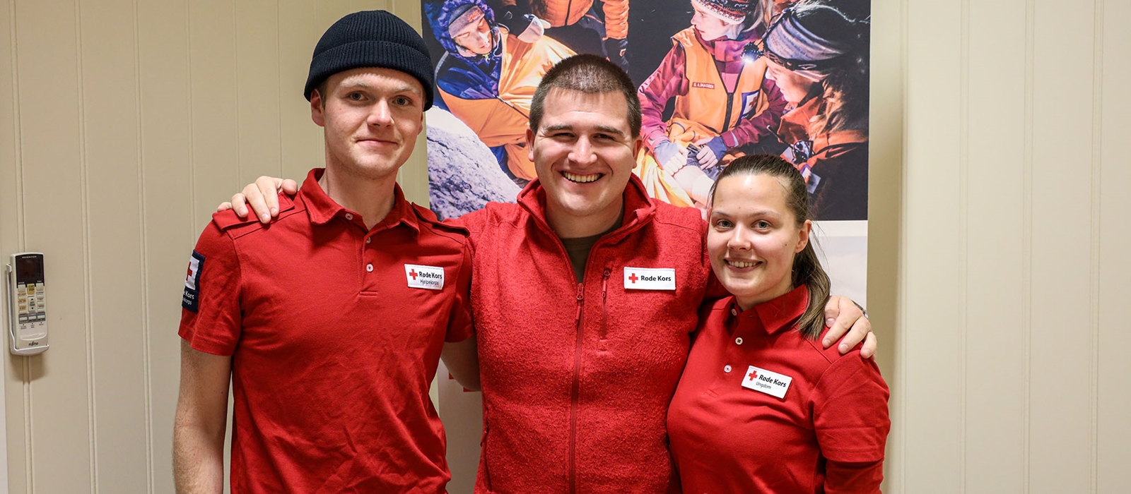 Tre uniformerte frivillige fra Røde Kors står sammen og smiler til kamera.