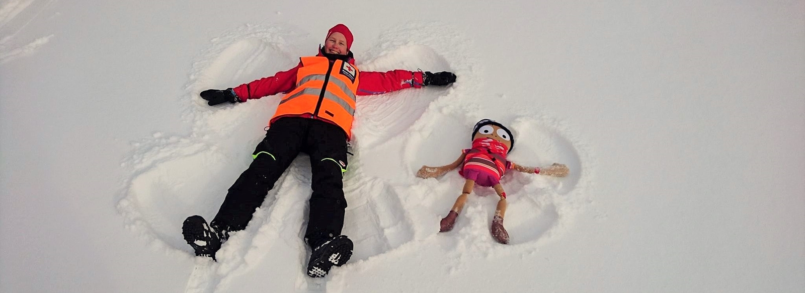 En frivillig i hjelpekorpsuniform og dukken Henry lager engler i snøren