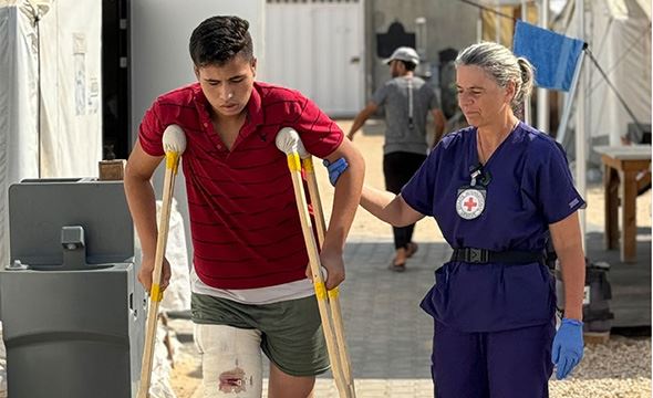 En kvinne hjelper en ung mann som er skadet og går på krykker. 