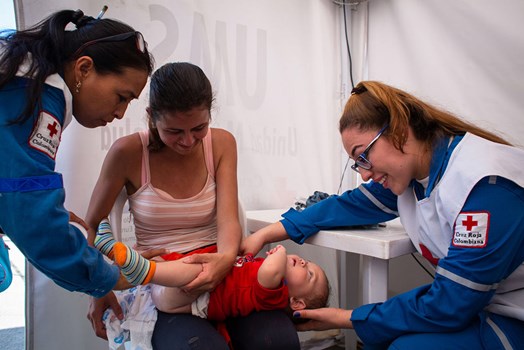 A mother holds her young daughter whilst Red Cross staff examine her (Colombian/Venezuelan border)