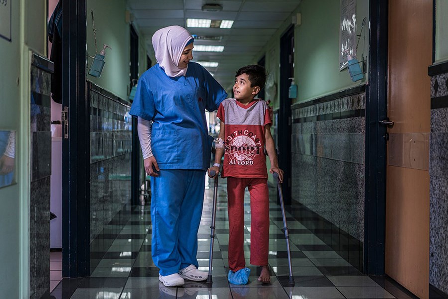 Young boy in hospital walking along with nurse