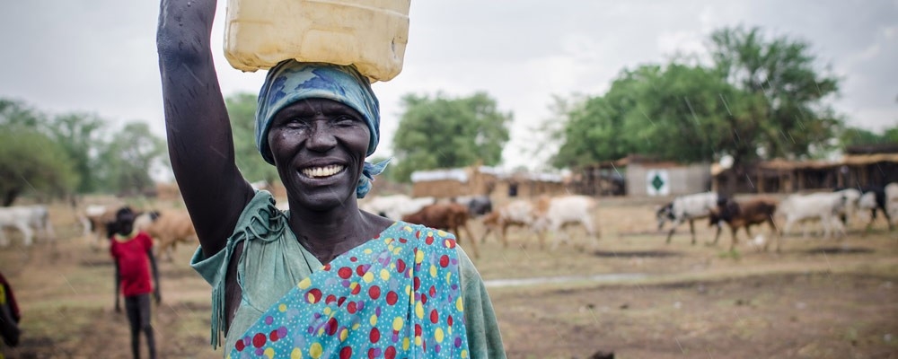 A woman smiles as she carries a container full of safe drinking water