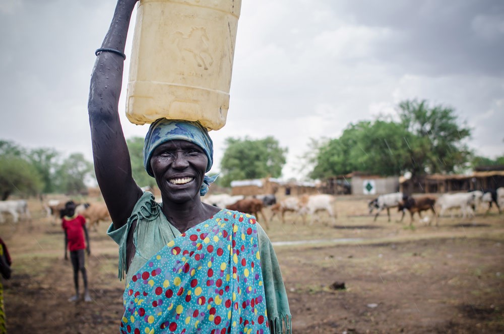 A woman smiles as she carries a container full of safe drinking water