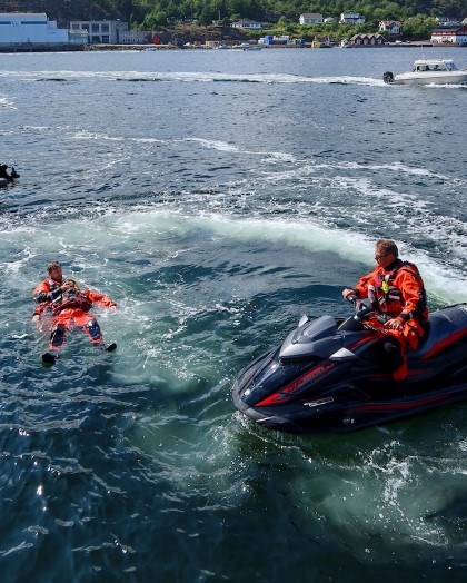 To menn i uniform i båt øver på å redde mann i havet