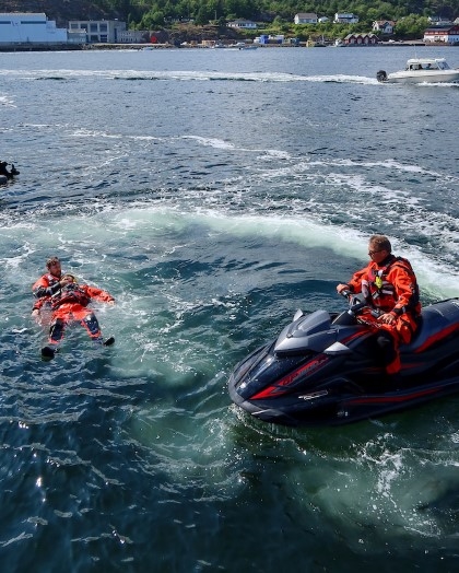 To menn i uniform i båt øver på å redde mann i havet