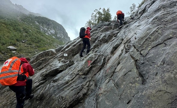 Frivillige fra Røde Kors bruker tau for å ta seg opp en bratt fjellside under en redningsaksjon.