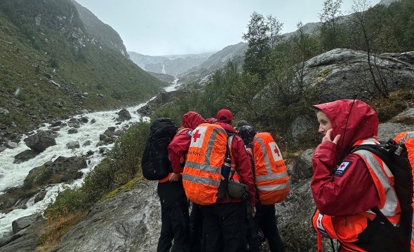 en gruppe frivillige leter etter en savnet person ute i fjellet under dårlige værforhold med vind og regn.