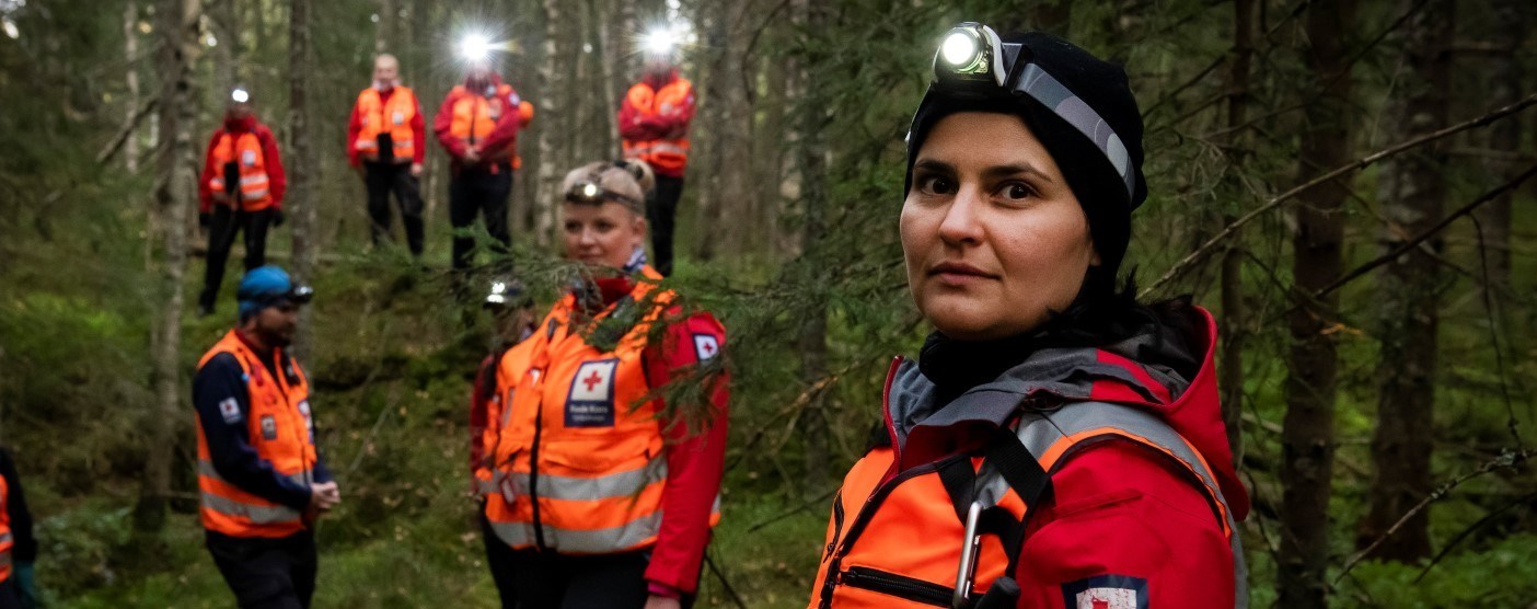 Illustrasjonbilde av en søk- og redningsaksjon i Oslo Røde Kors. Flere frivillige leter etter en savnet person i skogen på kveldstid.