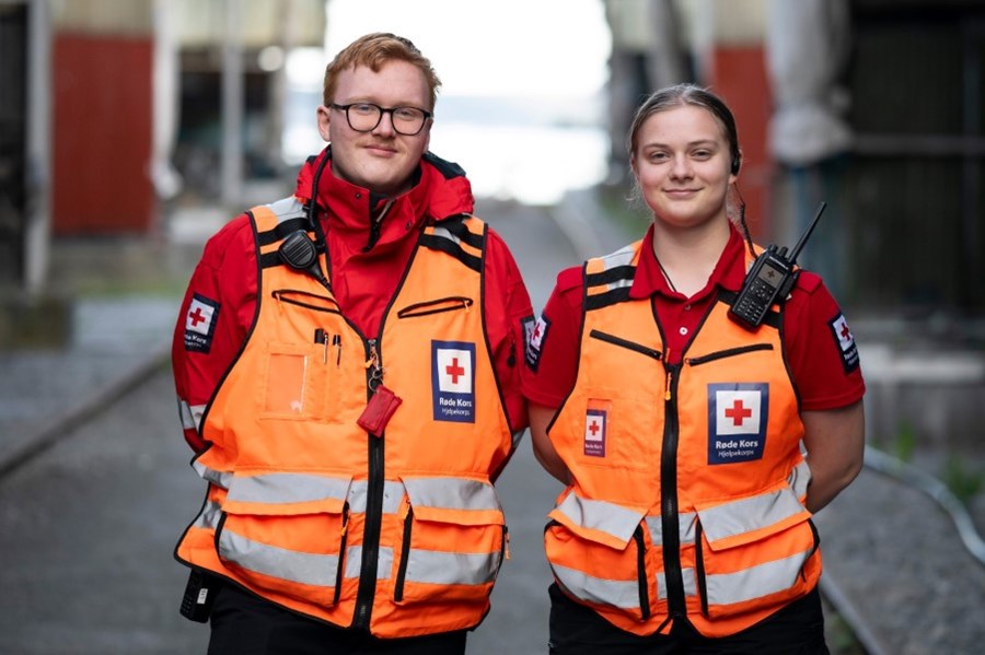To frivillige fra Drammen Hjelpekorps står oppstilt med uniform og oransje refleksvester. Det er en ung mann og en ung kvinne.