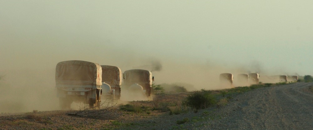 Flere små, hvite lastebilder kjører langs en støvete vei
