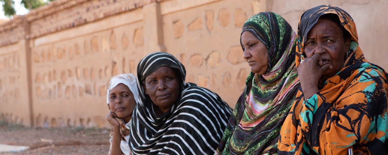 Fire kvinner sitter ute på bakken ved en mur.