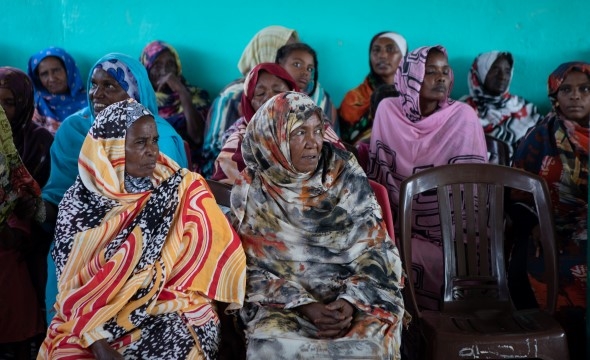 En gruppe kvinner sitter på plaststoler og venter på en helsesjekk ved en mobil helseklinikk.
