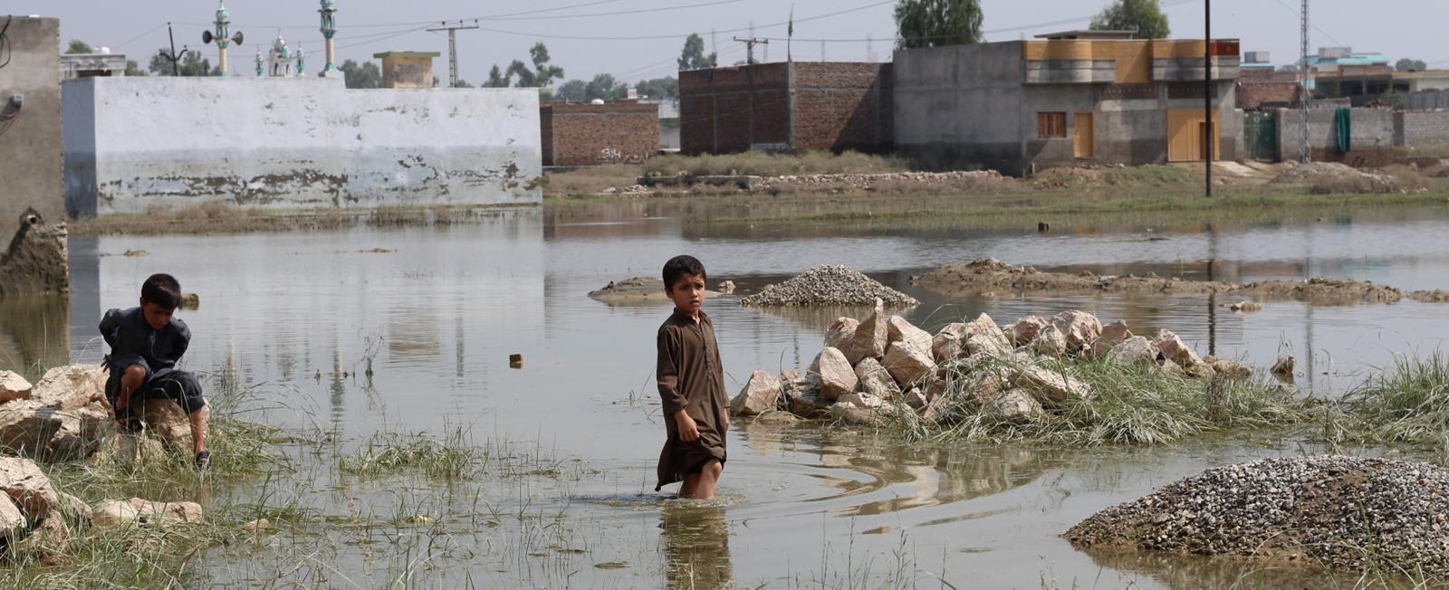 En liten gutt står med vann til knærne i  et oversvømt flomområde. 