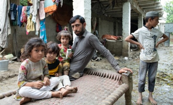 En mann sitter utenfor huset sitt med fire barn. Bakken er full av gjørme etter en flom.