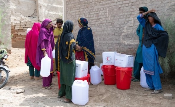 En gruppe mennesker står ute i skyggen etter å ha hentet vann og annet nødhjelpsutstyr.