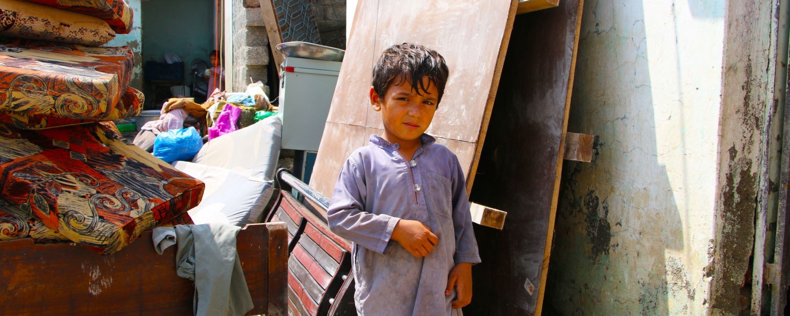 En liten gutt står i en bakgate omgitt av plater, møbler og byggemateriell