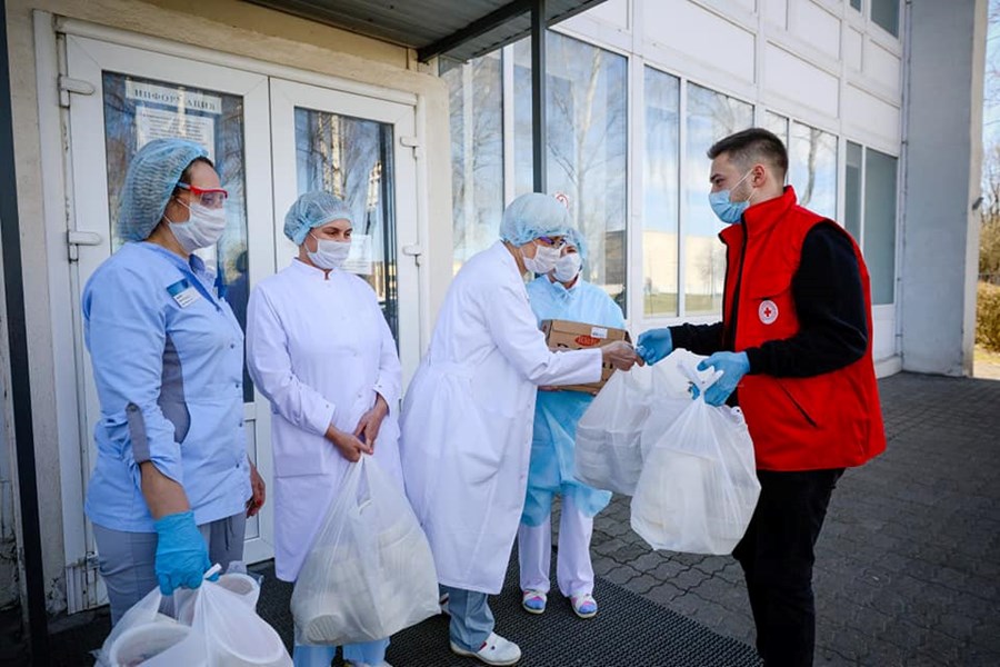 En mann fra Røde Kors overleverer mange bæreposer til tre personer i smittevernsutstyr.