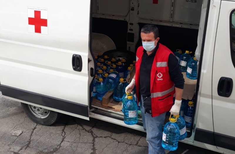 En mann med munnbind bærer vanndunker ut av en bil.