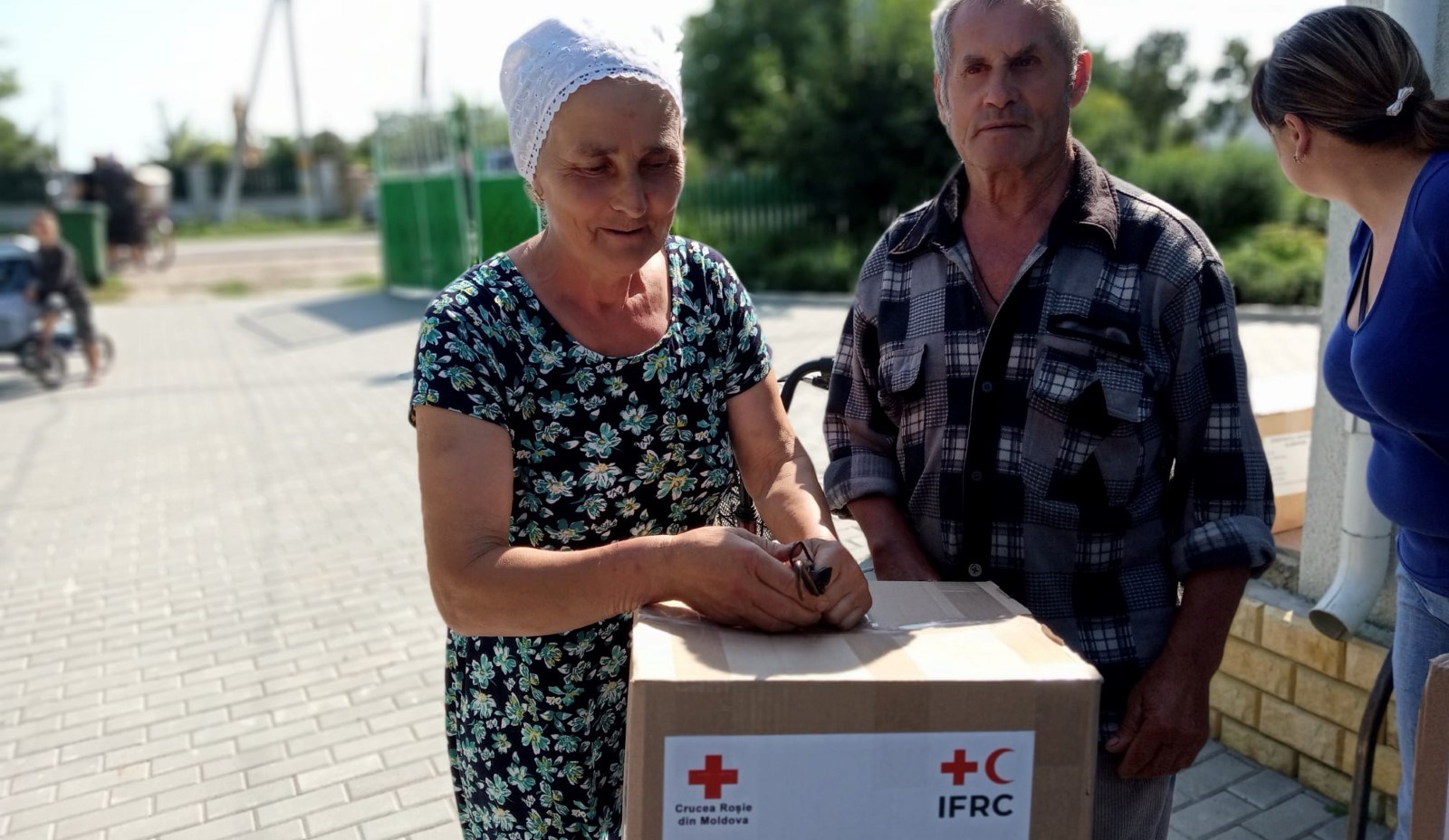 En eldre kvinne og mann lener seg på en pappkasse med logoen til Røde Kors og ICRC.