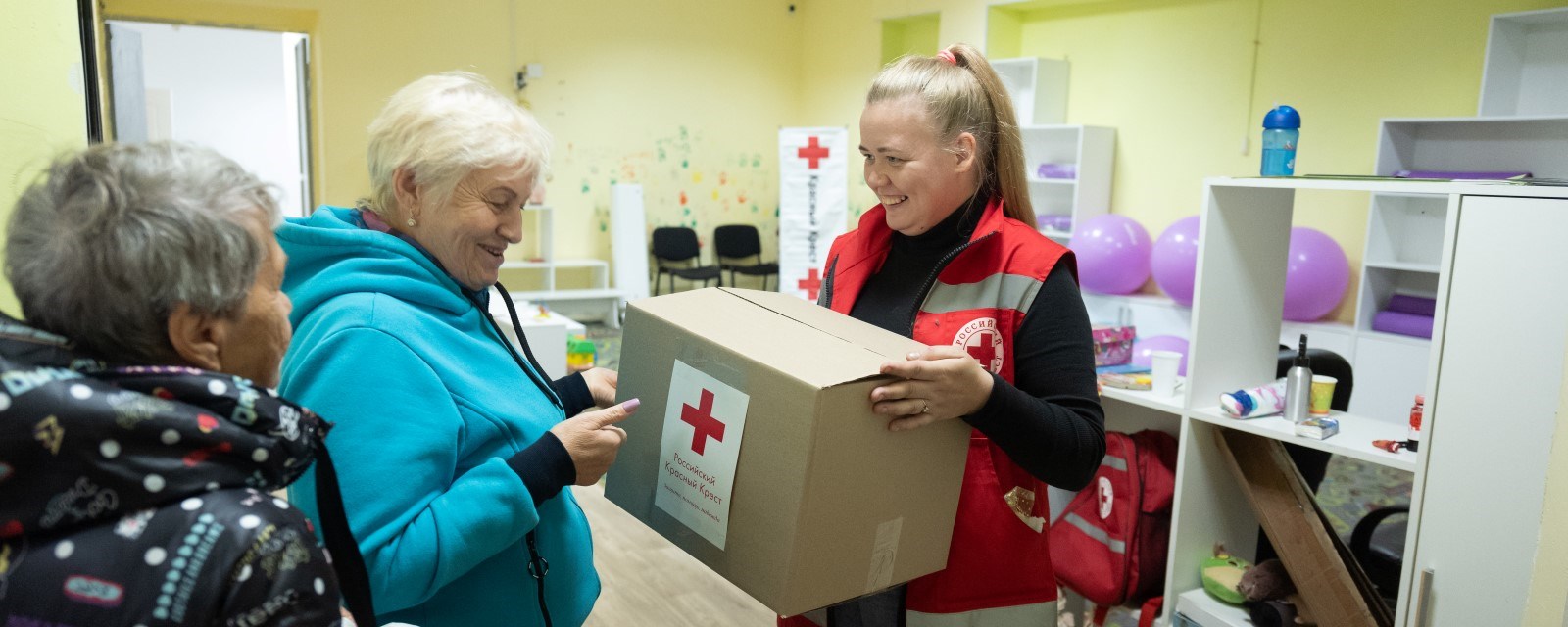 En kvinne fra Røde Kors gir en eske med nødhjelp til to eldre kvinner