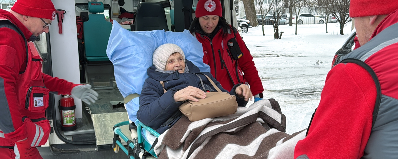 En eldre dame blir trillet inn i en ambulanse med assistanse fra Røde Kors