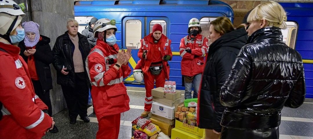 Frivillige fra Røde Kors står nede i en metrostasjon foran esker med mat og andre nødvendigheter.