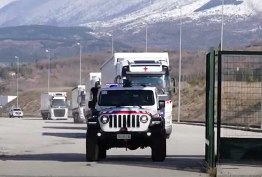 Hvite lastebiler med nødhjelp kjører gjennom port