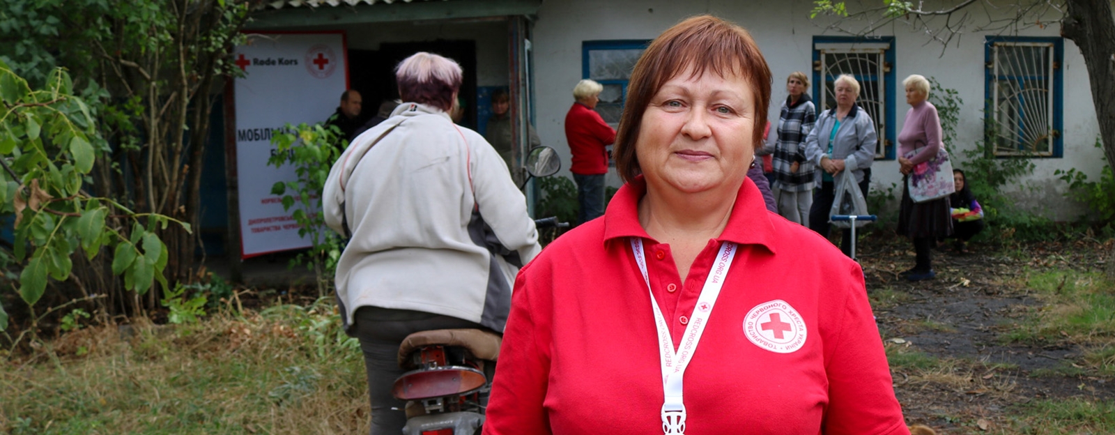 Dame i rød Røde Kors genser ser i kamera ute.