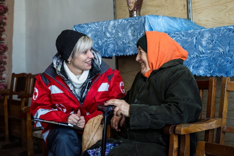 En kvinne fra Røde Kors og en eldre kvinne sitter på hver sin stol og snakker sammen.