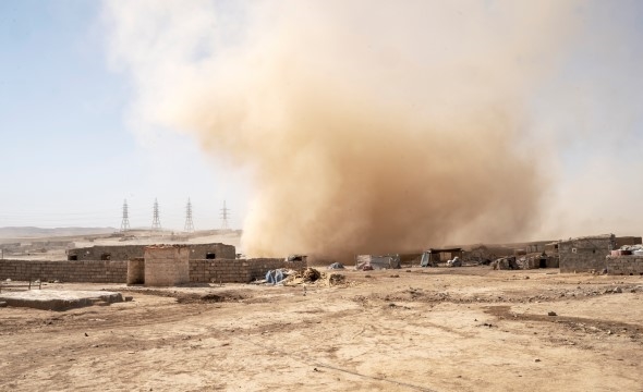 Rød sand virvler opp i lufta under en sandstorm.