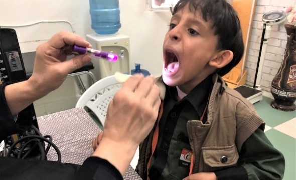 En liten gutt gaper opp munnen mens en lege lyser ned i halsen hans med lommelykt.