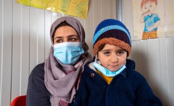 En kvinne med munnbind sitter ved siden av sønnen sin