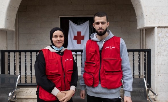 En ung kvinne og en ung mann står oppstilt med røde vester. De er frivillige i Røde Kors.