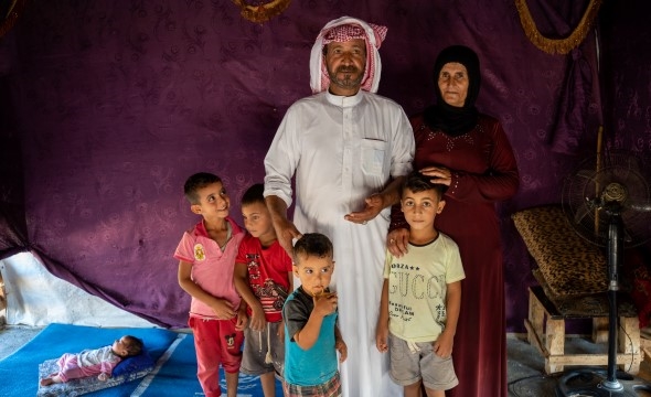 En far og mor står sammen med fem av barna deres inne i et telt i en leir for flyktninger.