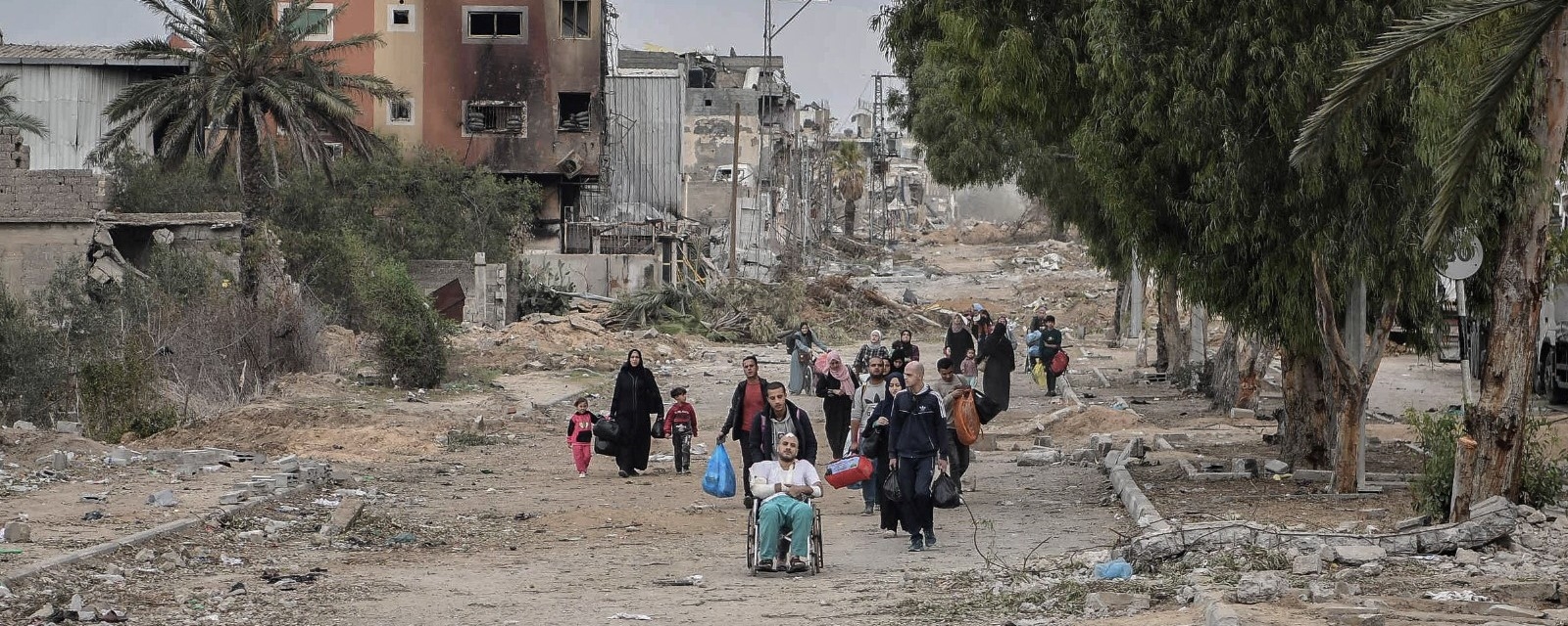 En gruppe mennesker på flukt går gjennom en gate, bærende på noen få personlige eiendeler. Det er ødelagte hus på alle kanter.