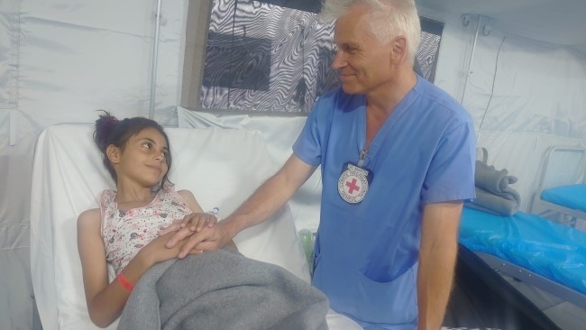 En ung jente ligger i en sykeseng og smiler til en mann i operasjonsklær