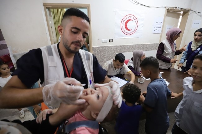 En mann fra palestinsk Røde Halvmåne gir en jente dråper med poliovaksine