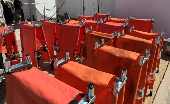 Sammenslåtte sykebårer står oppstilt utenfor en bygning. De er trukket i oransje kledning.