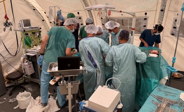 En gruppe leger og sykepleiere står rundt et operasjonsbord og jobber for å redde en skadet pasient.