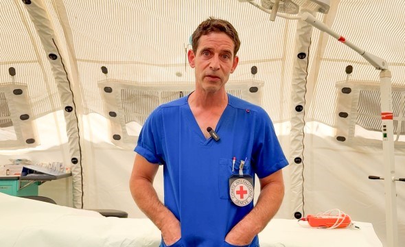 En mannlig operasjonssykepleier står i et tomt operasjonsrom med blå uniform.