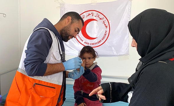 En mannlig lege fra Palestinsk Røde Halvmåne undersøker en liten jente på helseklinikken.