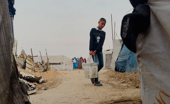 Mahmoud Sultan bærer en bøtte til teltet sitt.