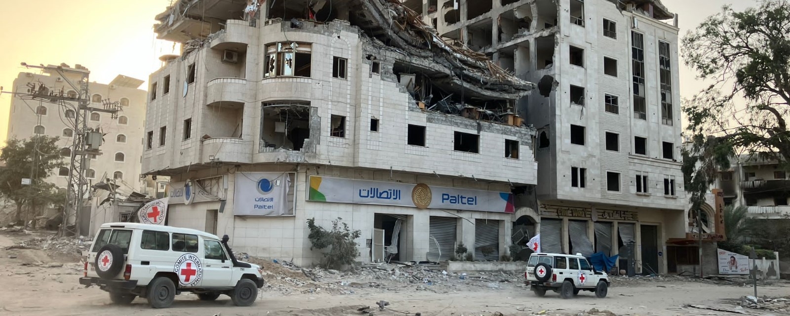 To bilder fra Røde Kors kjærer forbi en utbombet bygning