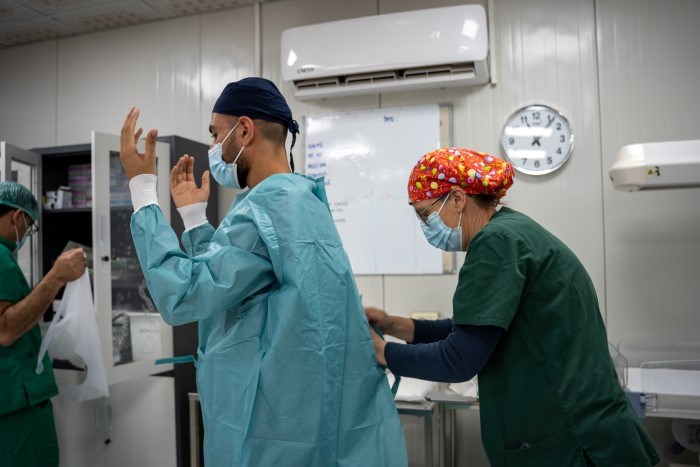 En sykepleier hjelper en kirurg med å ta på operasjonstøy