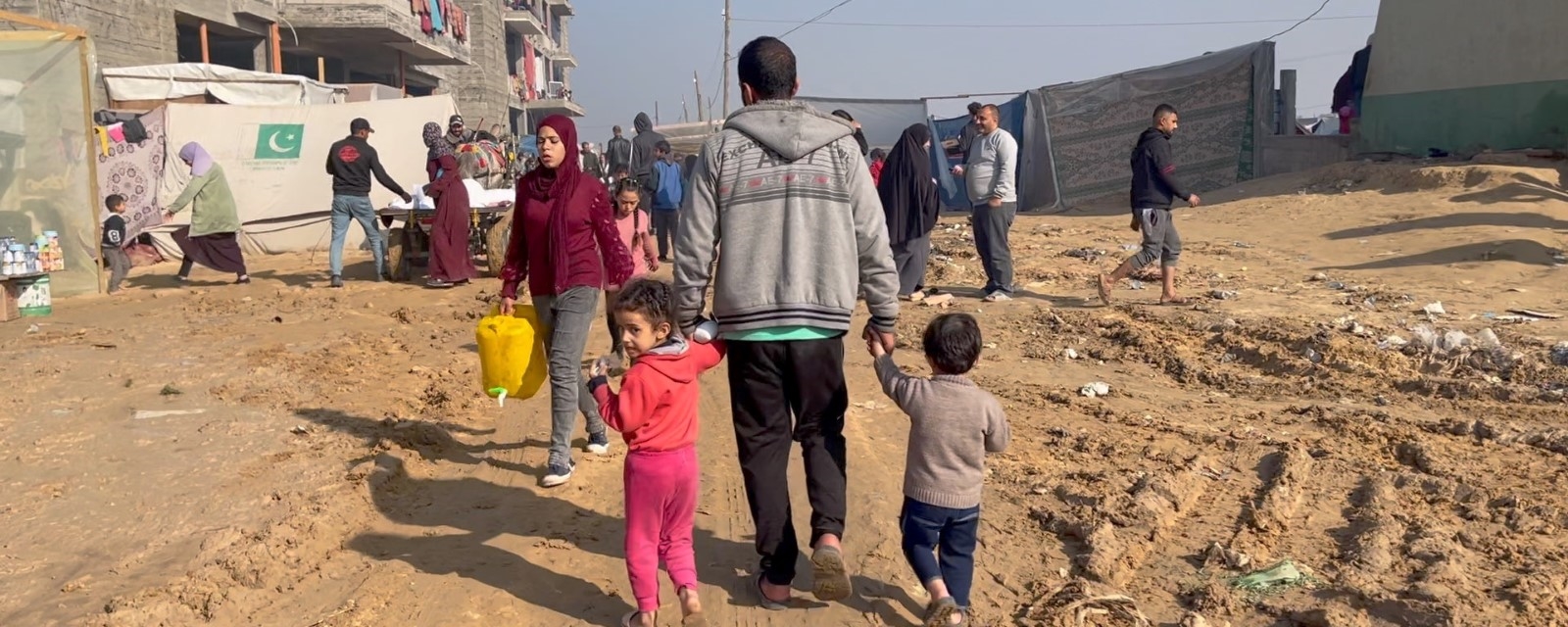 En far med to små barn går på en jordvei i Rafa