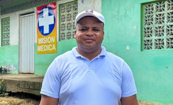 En mann med blå t-skjorte står utenfor en helsepost i landsbyen Palambi.