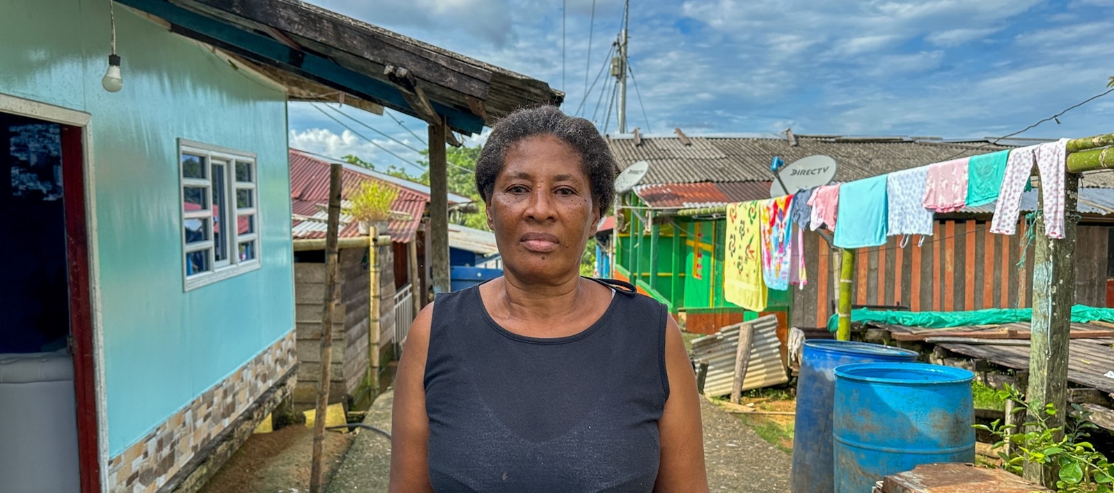En kvinne med blå singlet står foran et blått hus i en liten landsby.