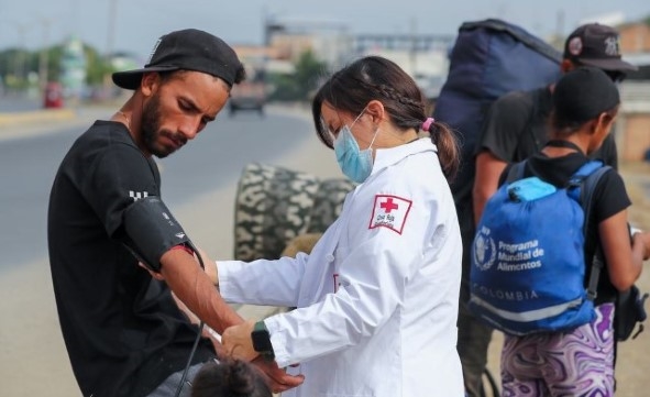 En dame med hvit legefrakk tar blodtrykket på en mannlig flyktning.