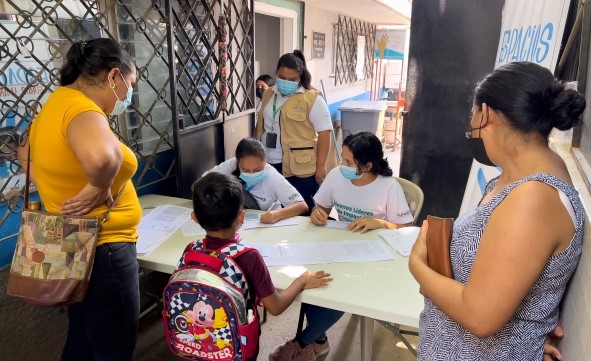 En kvinne og en liten gutt står foran et bord og venter på en helsesjekk.